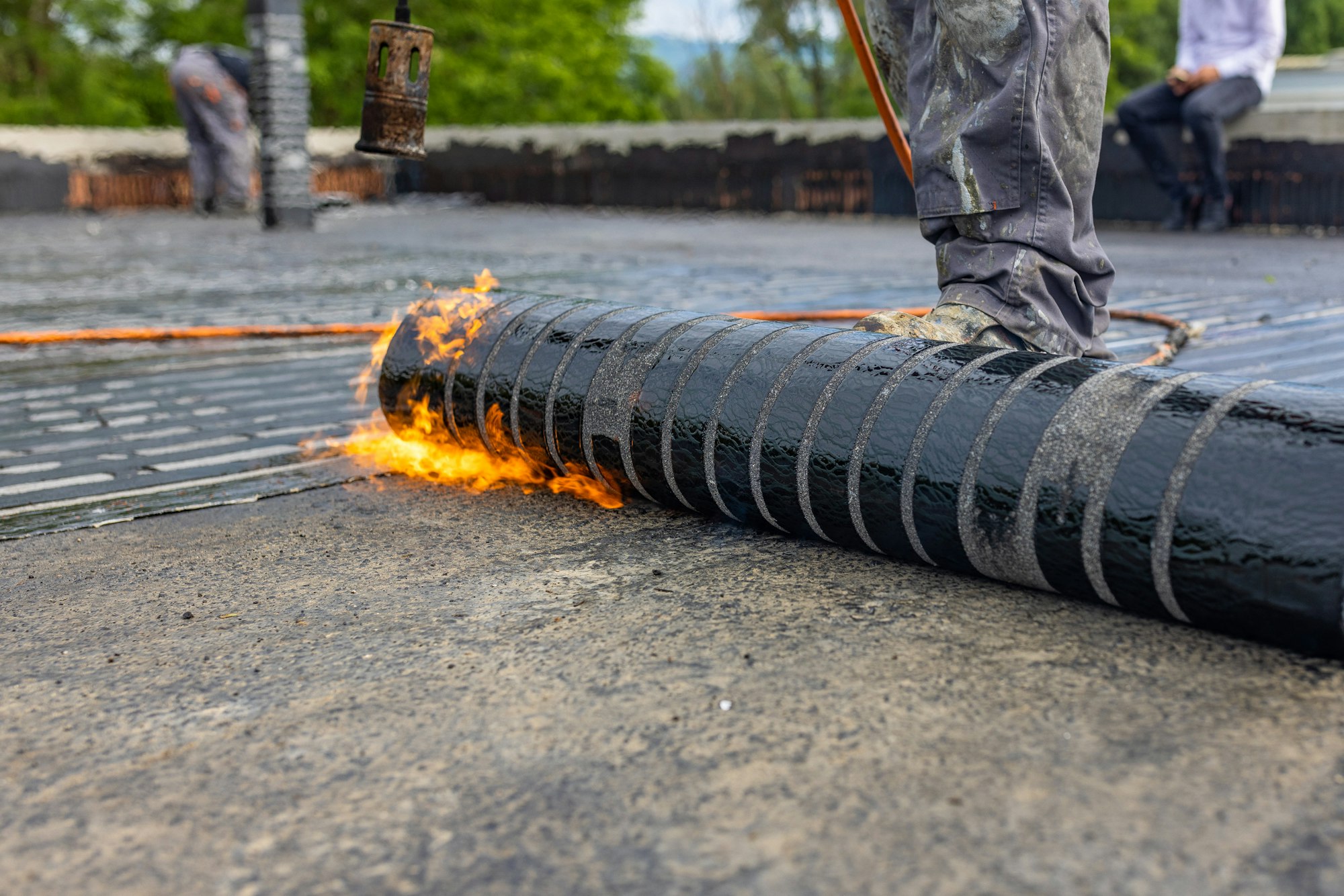 Workers placing a vapor barrier on the roof using a propane gas torch for welding bitumen sheets